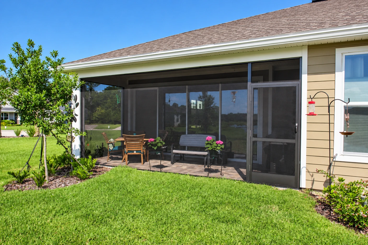 Screened patio enclosure attached to a house, with dark mesh walls, a seating area, and a green lawn.