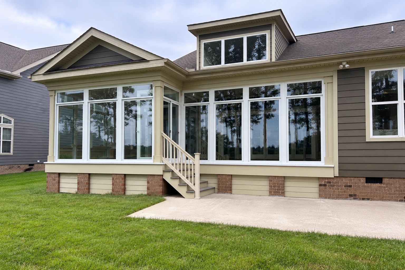 Exterior view of a house with a large white-framed sunroom addition and steps leading to the lawn.